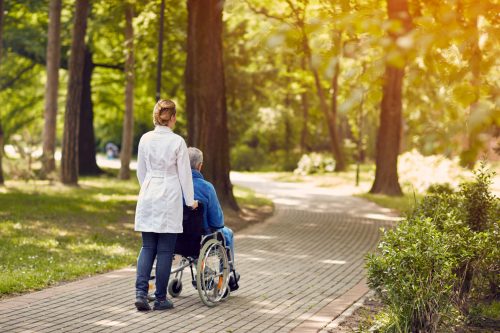 nurse helping elderly man on wheelchair outdoor